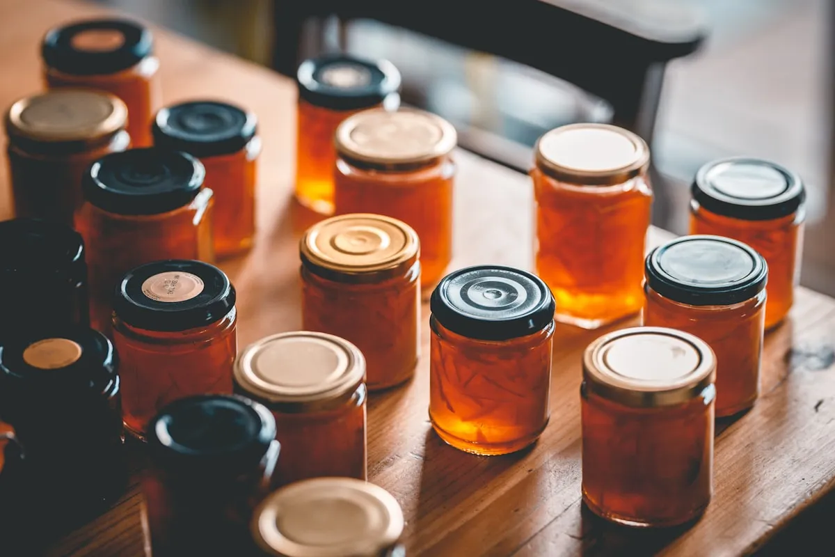 Rows of homemade marmalade jars with metal lids arranged on a wooden table in warm light