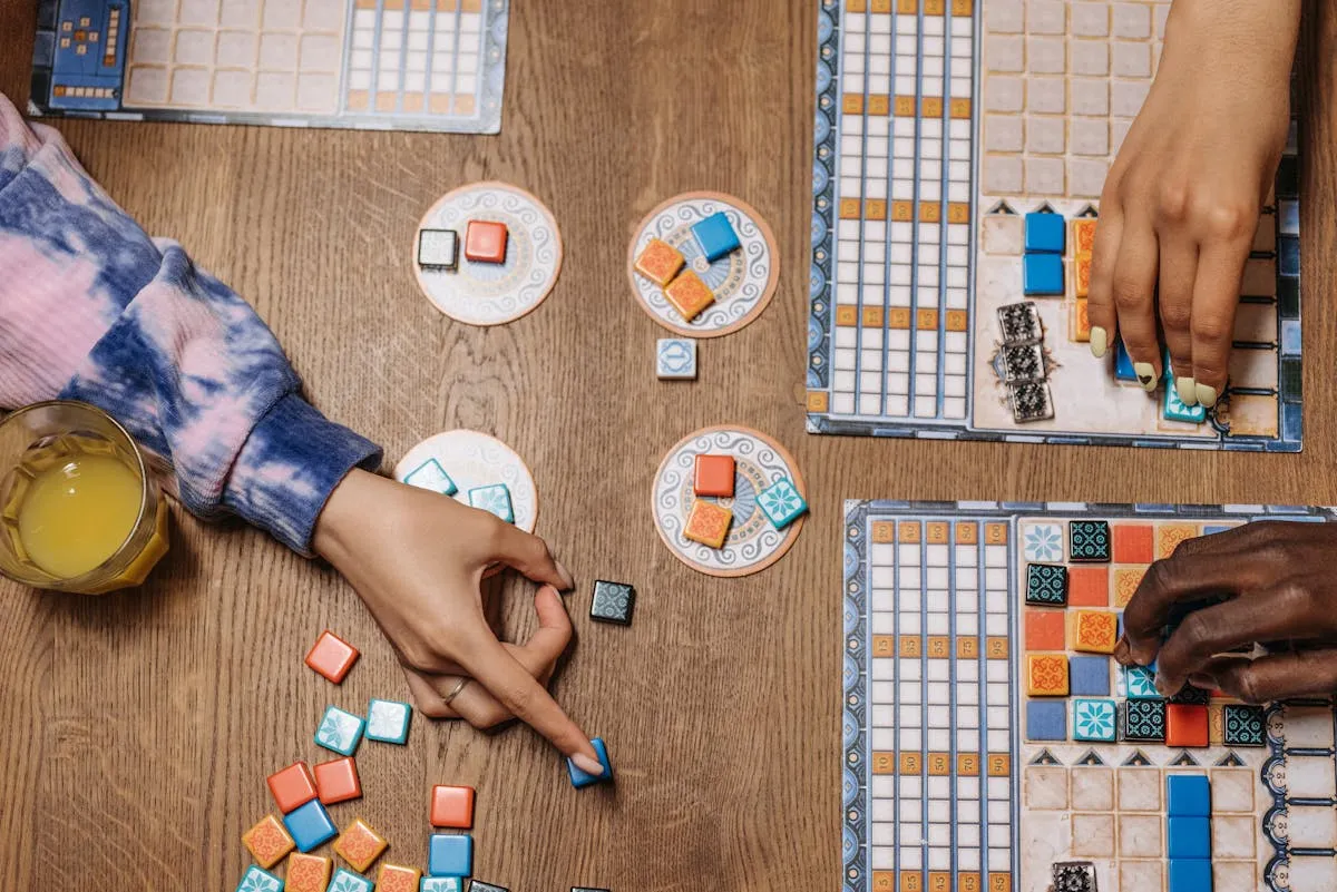 Overhead view of hands placing colorful tiles and game pieces on player boards during a tabletop game session