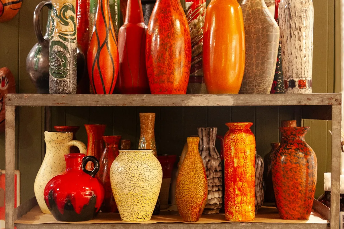 Two shelves of brightly glazed handmade ceramic vases and jugs arranged on a metal shop rack