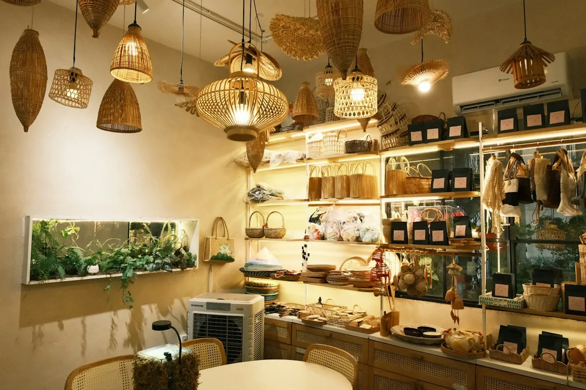 A small boutique of the kind that takes consignment, lit by woven rattan pendant lamps, its backlit shelves stocked with handmade baskets, bags and packaged goods
