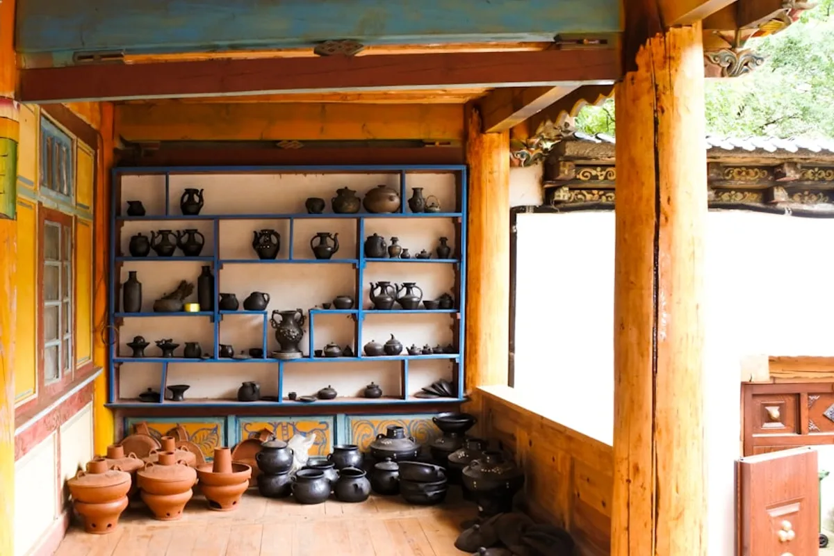 A rustic pottery workshop with hand-thrown clay pots on blue-painted shelving and rows of terracotta pots on the floor