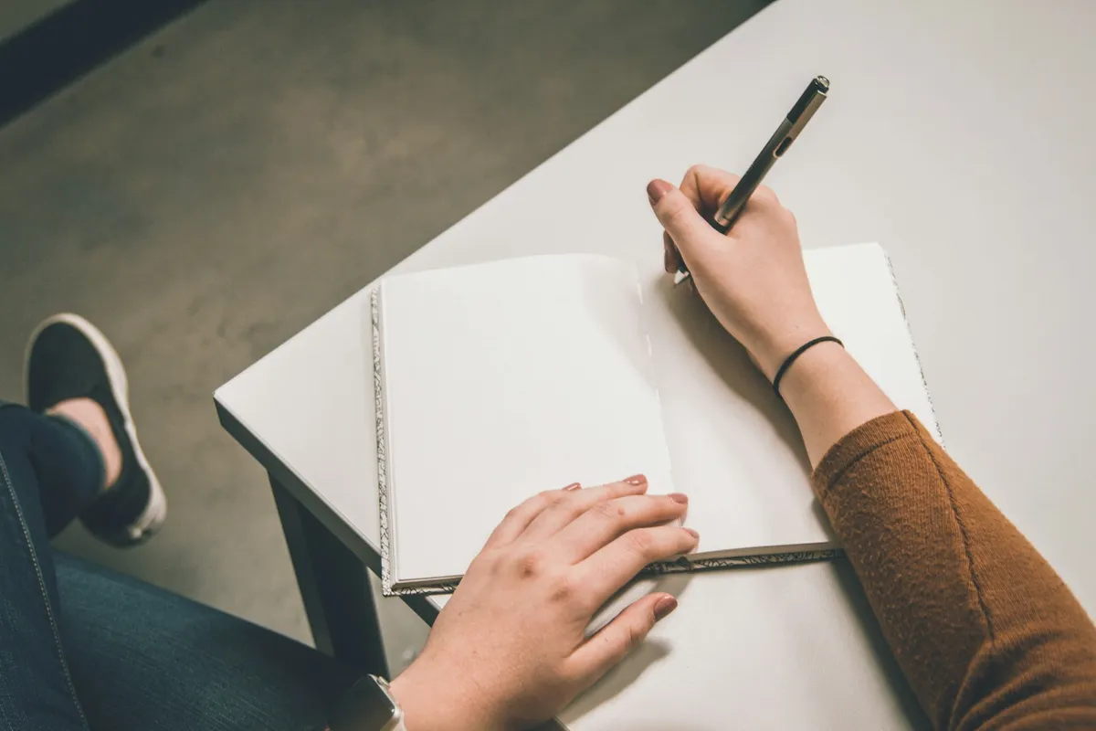 A maker at a white desk with a pen over the blank pages of an open notebook, about to write up an order