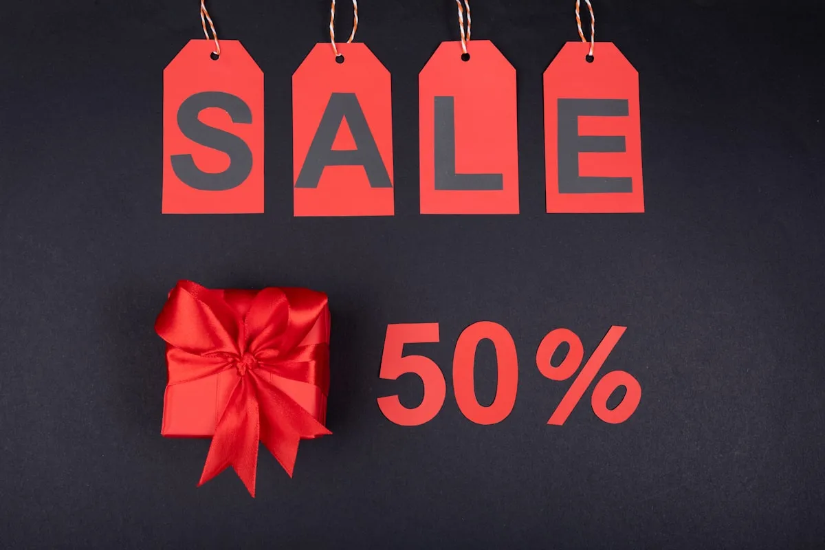 Four red price tags spelling "SALE" hung above a red ribboned gift box and a large red "50%" on a dark background