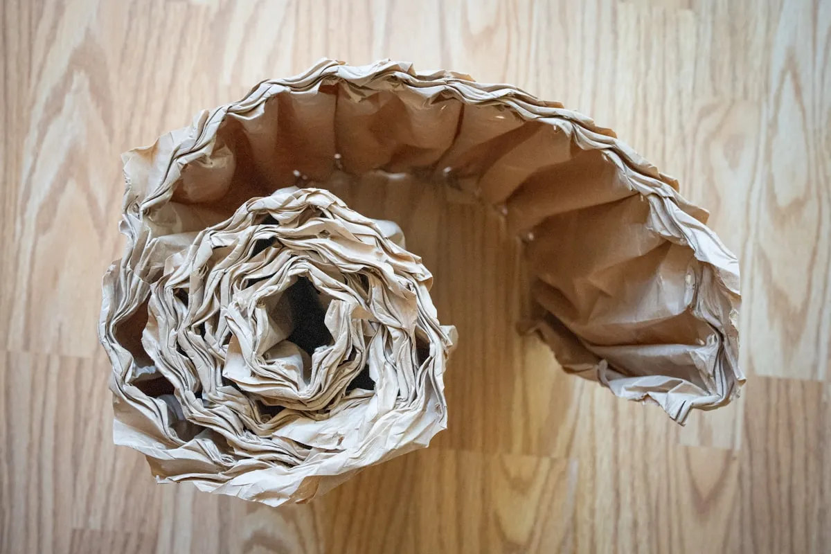Overhead view of a partly unrolled coil of crinkled kraft paper void fill on a pale wooden work surface