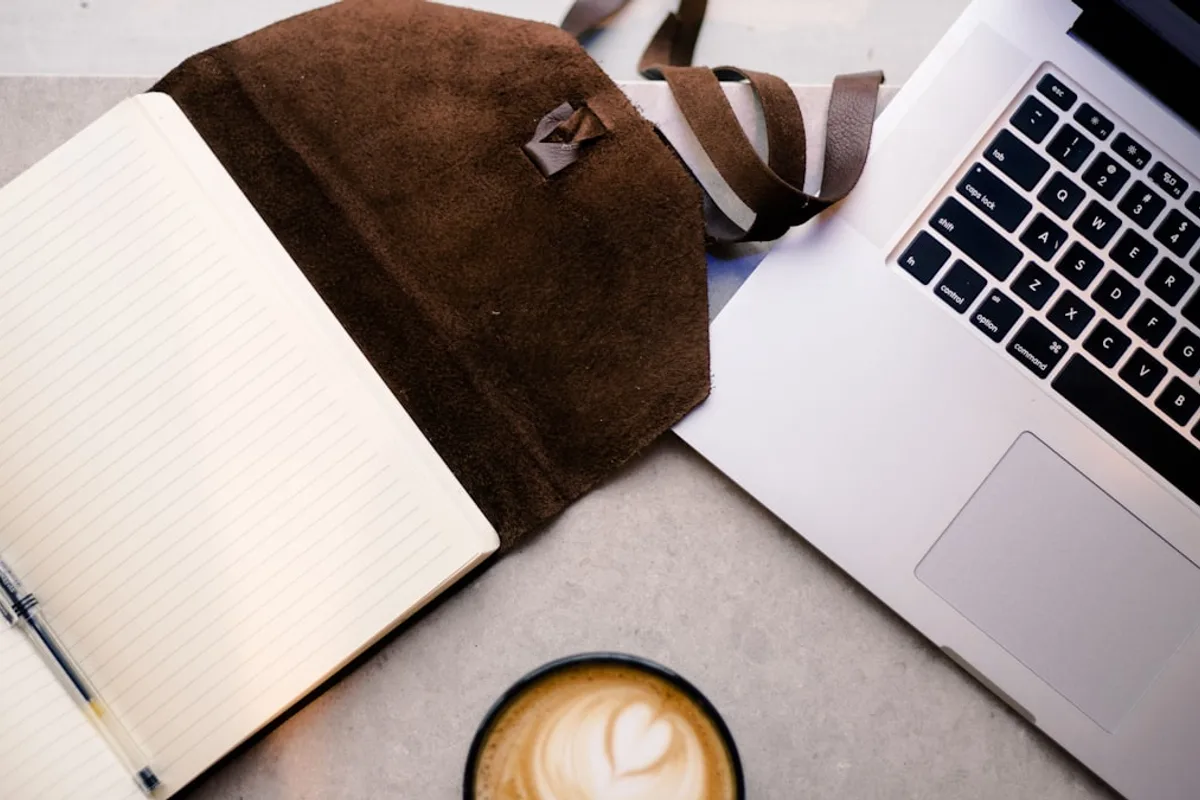A notebook, pen, laptop, and coffee on a desk — a workspace for working through Etsy Ads break-even math