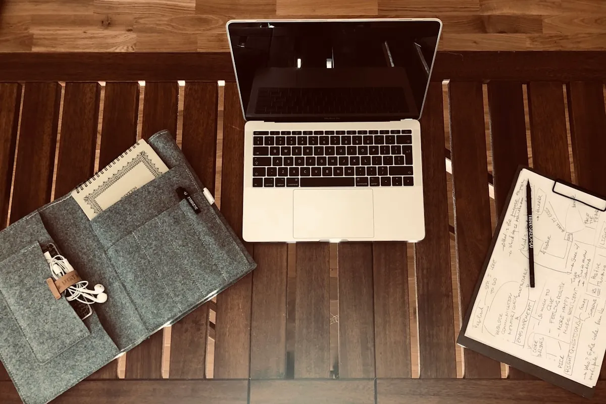 Overhead view of a small-business planning desk — open laptop, gray felt notebook organizer, and a clipboard with a hand-drawn flowchart sketching out a business categorization plan