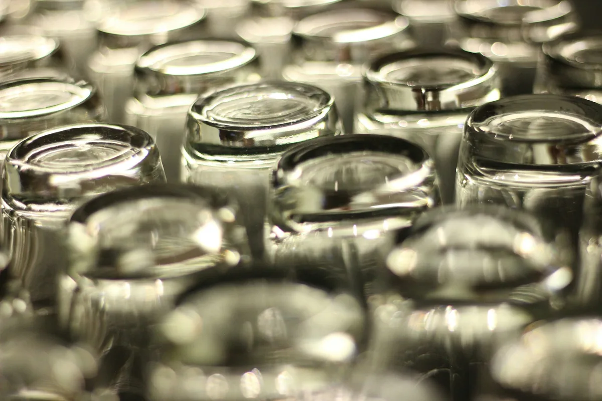 Dozens of empty clear glass jars packed upright in tight rows, receding out of focus toward the back
