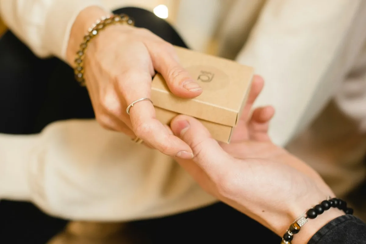 Close-up of a seller placing a small kraft gift box into a customer's open palm — the moment a handmade product leaves the maker's hands