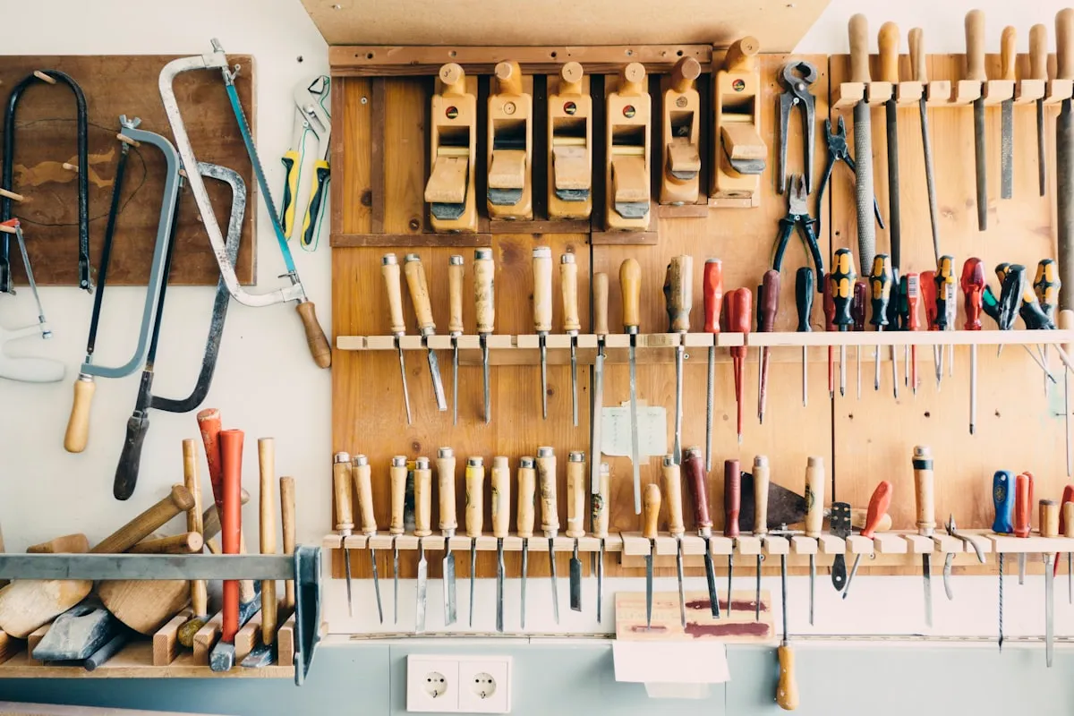 An organized workshop tool wall with rows of chisels, planes, saws, and files in wooden racks against a pine-paneled wall