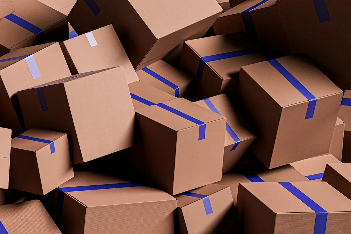 A pile of plain brown cardboard shipping boxes, each sealed with a strip of blue tape