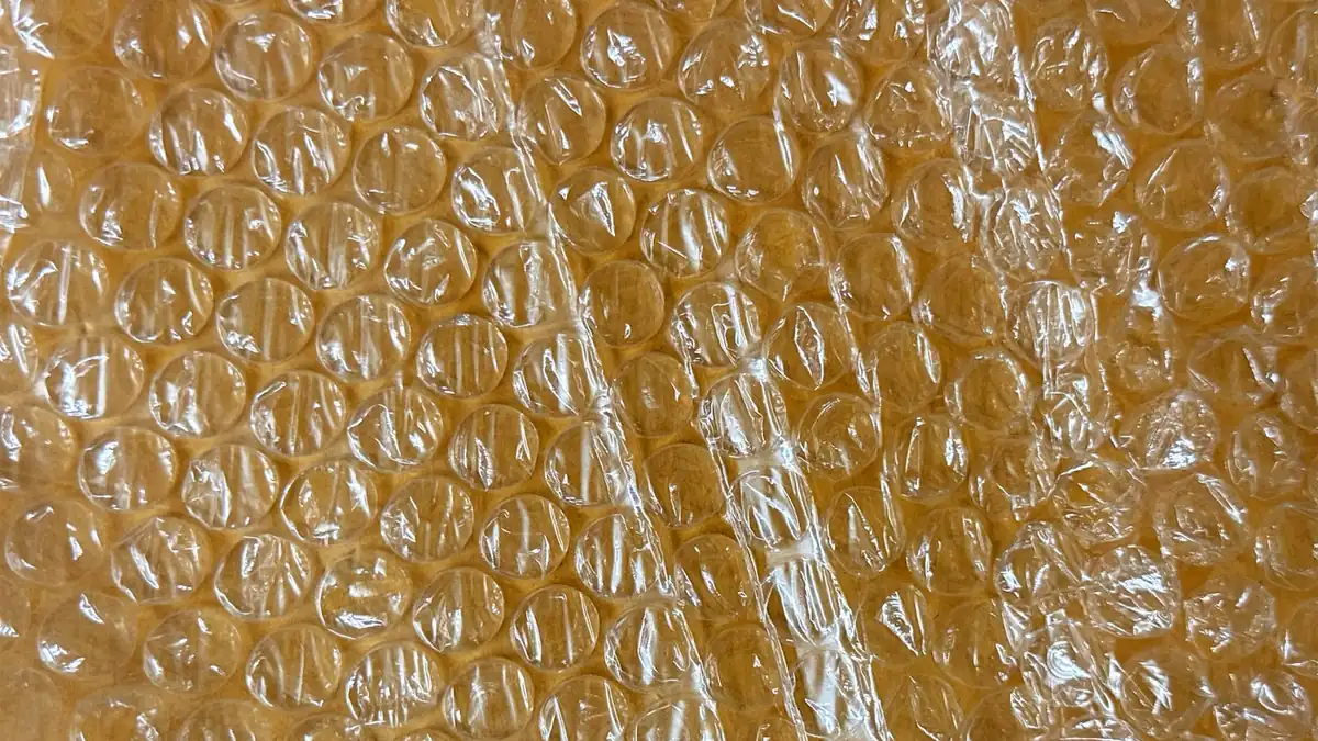Close-up of clear air-cellular bubble cushioning laid over a warm brown kraft surface, the material carriers specify for wrapping fragile items
