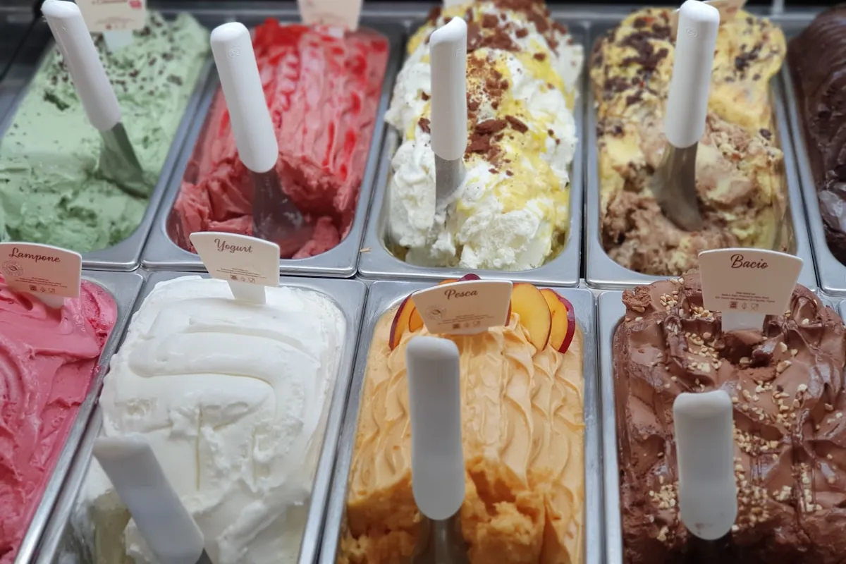 Rows of colorful gelato in a stainless display case, each tub marked with a flavor card