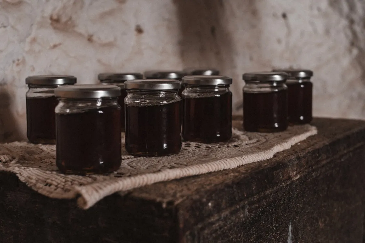 Rows of small half-pint jars of dark homemade jam arranged on a lace cloth on a rustic wooden surface