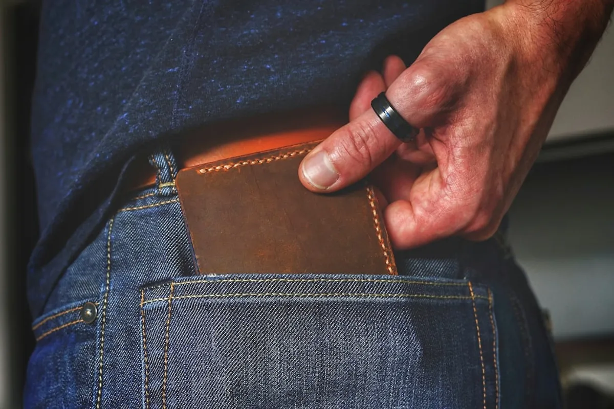 A hand sliding a handmade brown leather bifold wallet into the back pocket of a pair of jeans