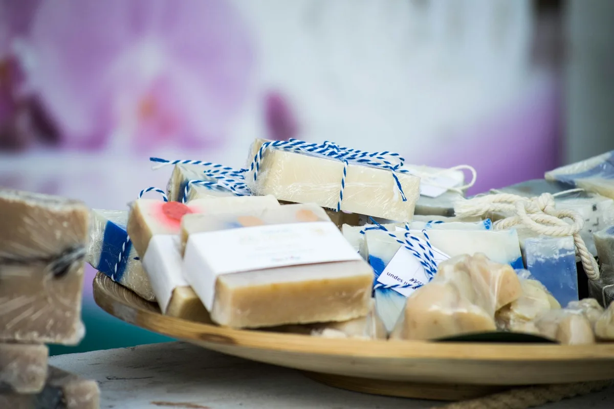 A wooden tray piled with wrapped and labeled bars of handmade cold-process soap in cream, blue, and speckled colors