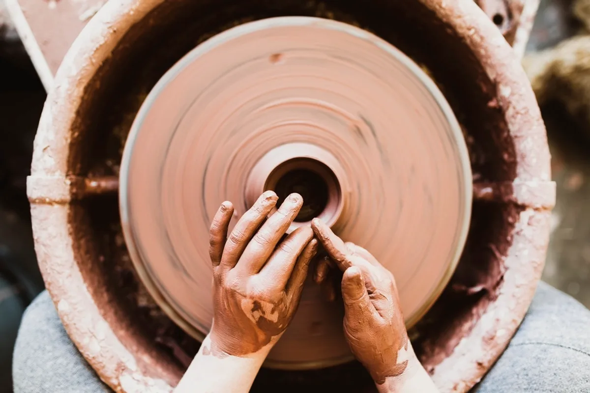 A potter's hands shaping wet clay on a spinning wheel — a single maker working at small-batch scale, not a factory floor