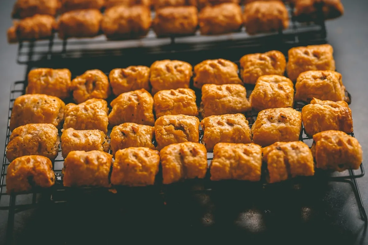 Two cooling racks of square golden-brown biscuit-style pastries fresh from a home oven, photographed in moody side light on a dark countertop