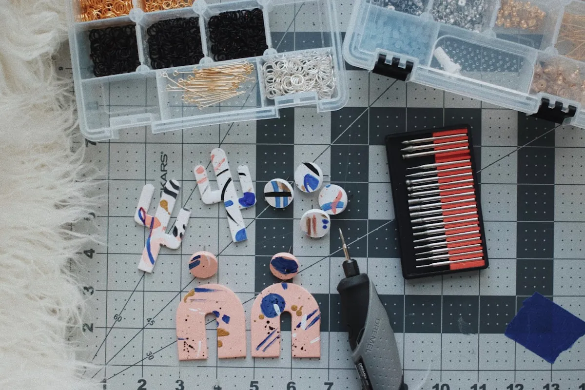 Overhead view of a polymer clay maker's cutting mat with colorful clay earring blanks, organizer boxes of jump rings and posts, and a rotary tool