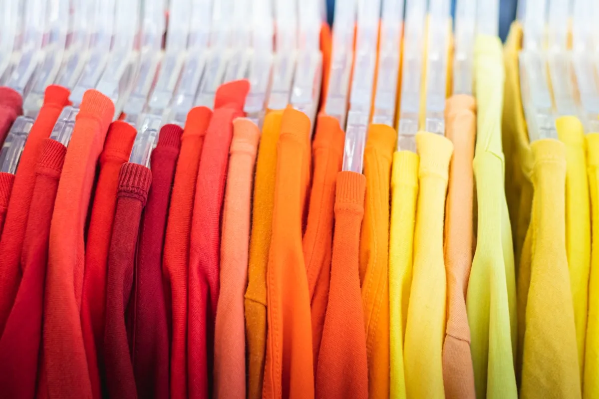 Colorful t-shirts in red, orange, and yellow hanging on clear plastic hangers on a clothing rack in a gradient arrangement
