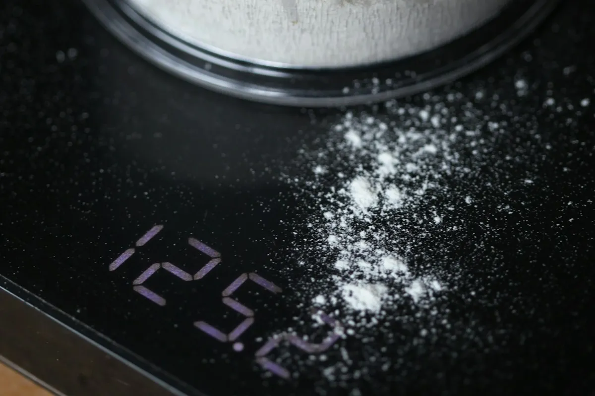 Close-up of a black digital scale reading 125.2, with white powder spilled across the platform beside the base of a clear canister